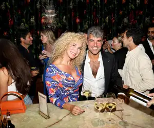 Gorgeous power couple Dani and Marina Alonso stand at the green onyx bar with wine pours.