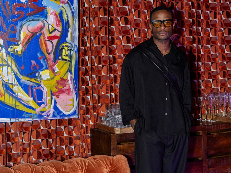 Black man posing in incredible outfit along Guell velvet draped wall next to Domingo Zapata painting.