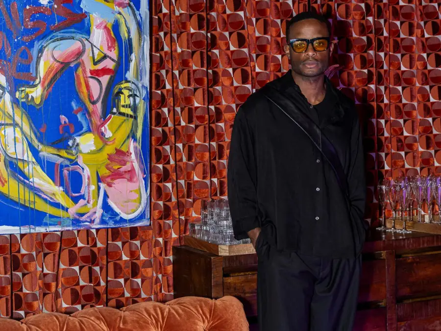Black man posing in incredible outfit along Guell velvet draped wall next to Domingo Zapata painting.